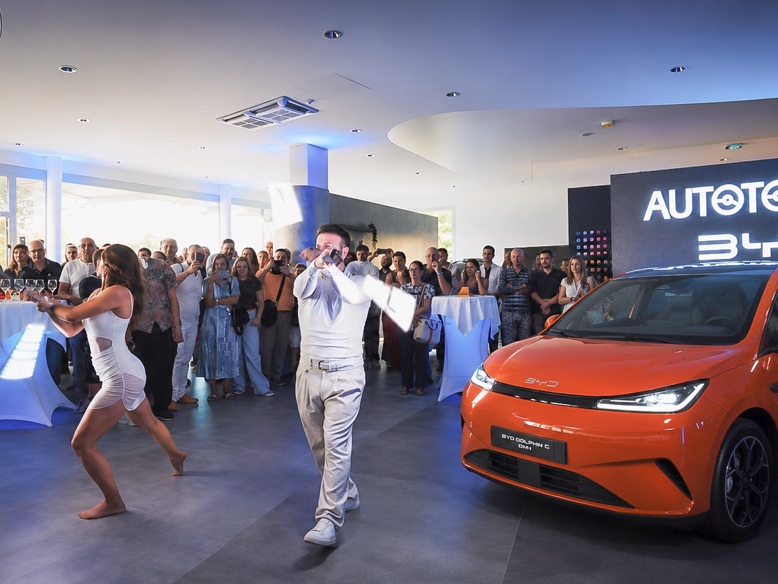Performance di danza e show visivo con bastoni luminosi a LED davanti a una vettura BYD arancione durante un evento di auto reveal in concessionaria.